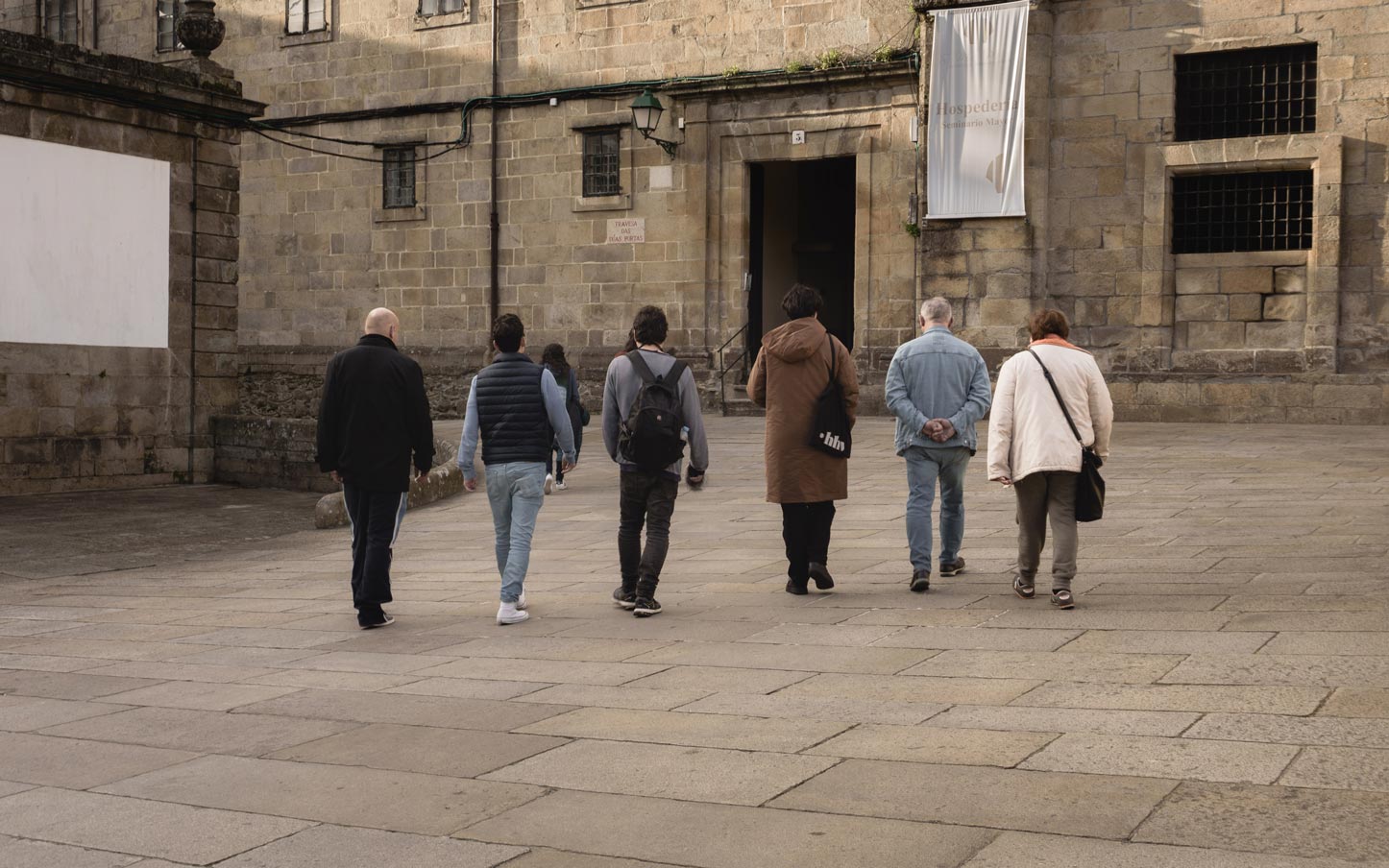 Vista de espalda de 6 personas caminando hacia la Hospedería de San Martín Pinario en Santiago