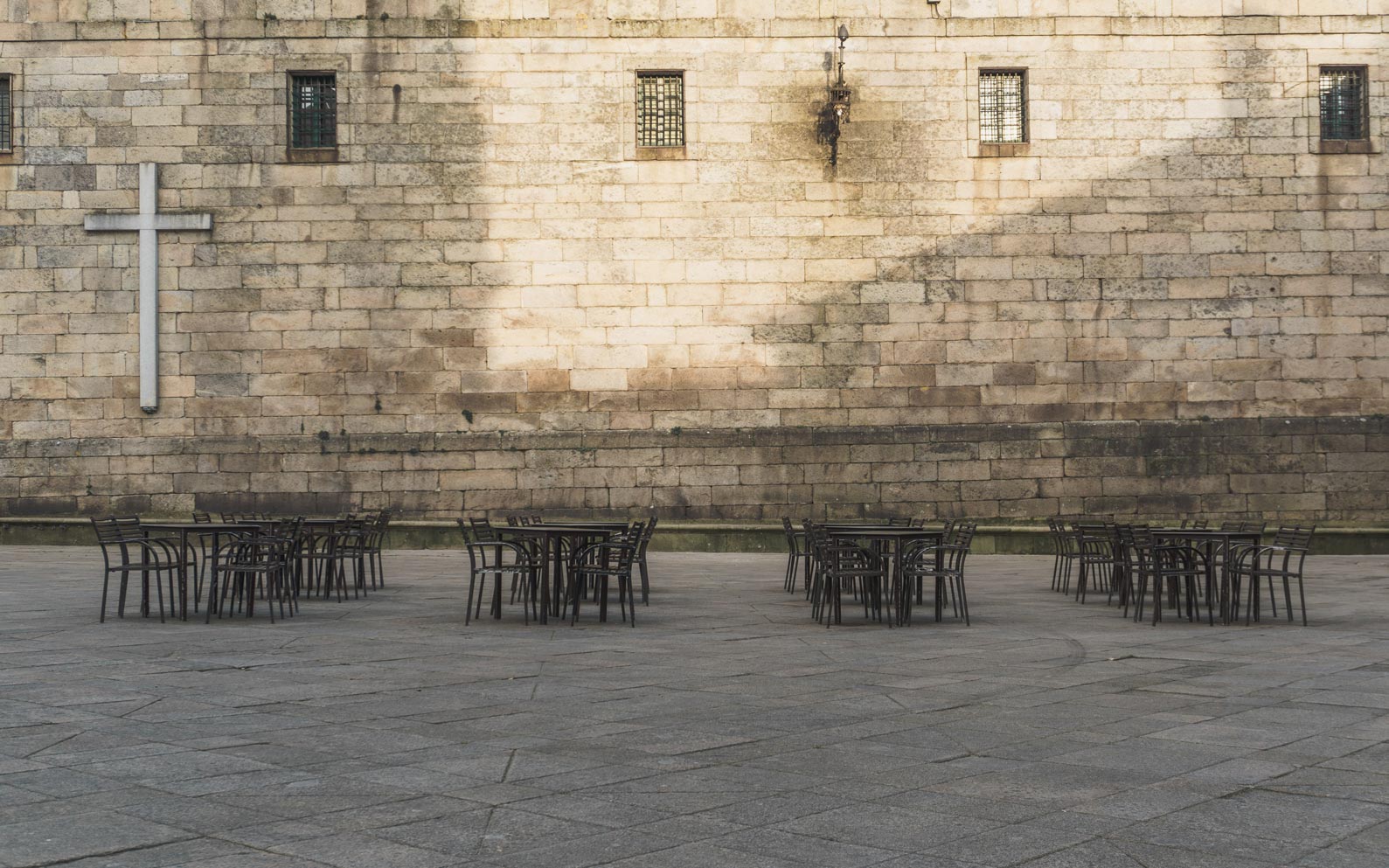 Mesas de hostelería vacías y cruz católica de fondo en la Plaza de Quintana dos Mortos.