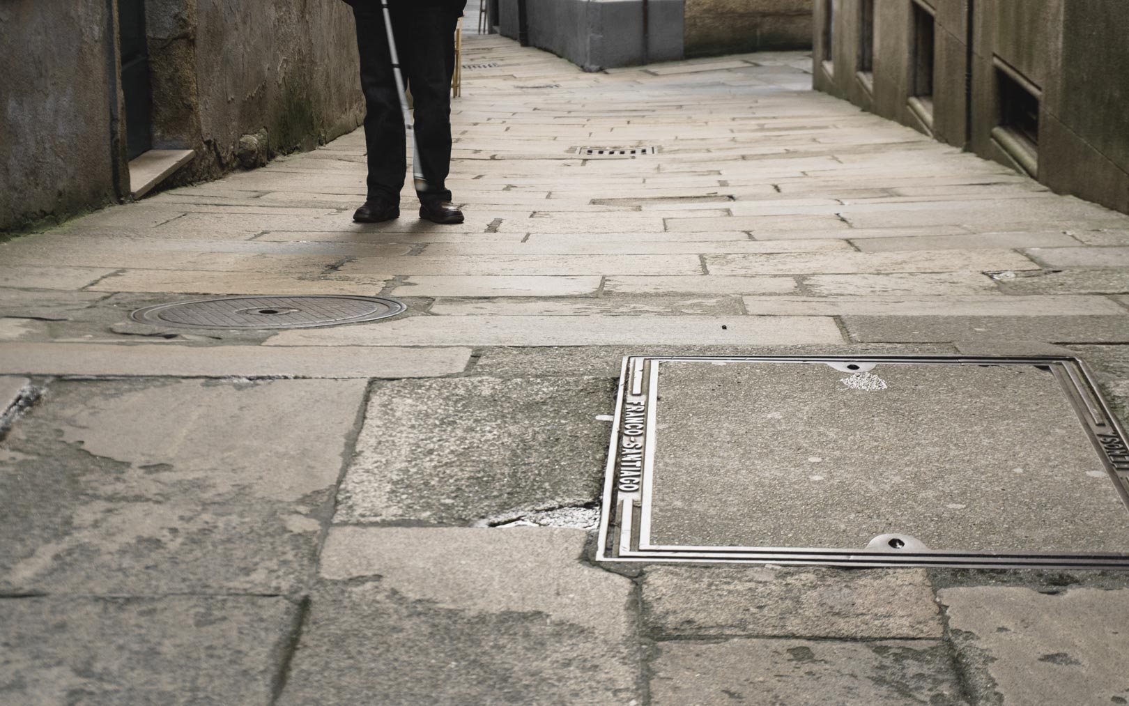 Enfoque de las piernas de una persona con bastón guía caminando en el casco antiguo de Santiago. 