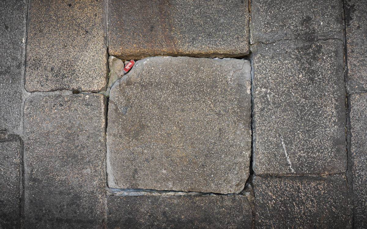 Pavimento lítico con huecos y desniveles en el que se observa incrustado un pequeño papel doblado.