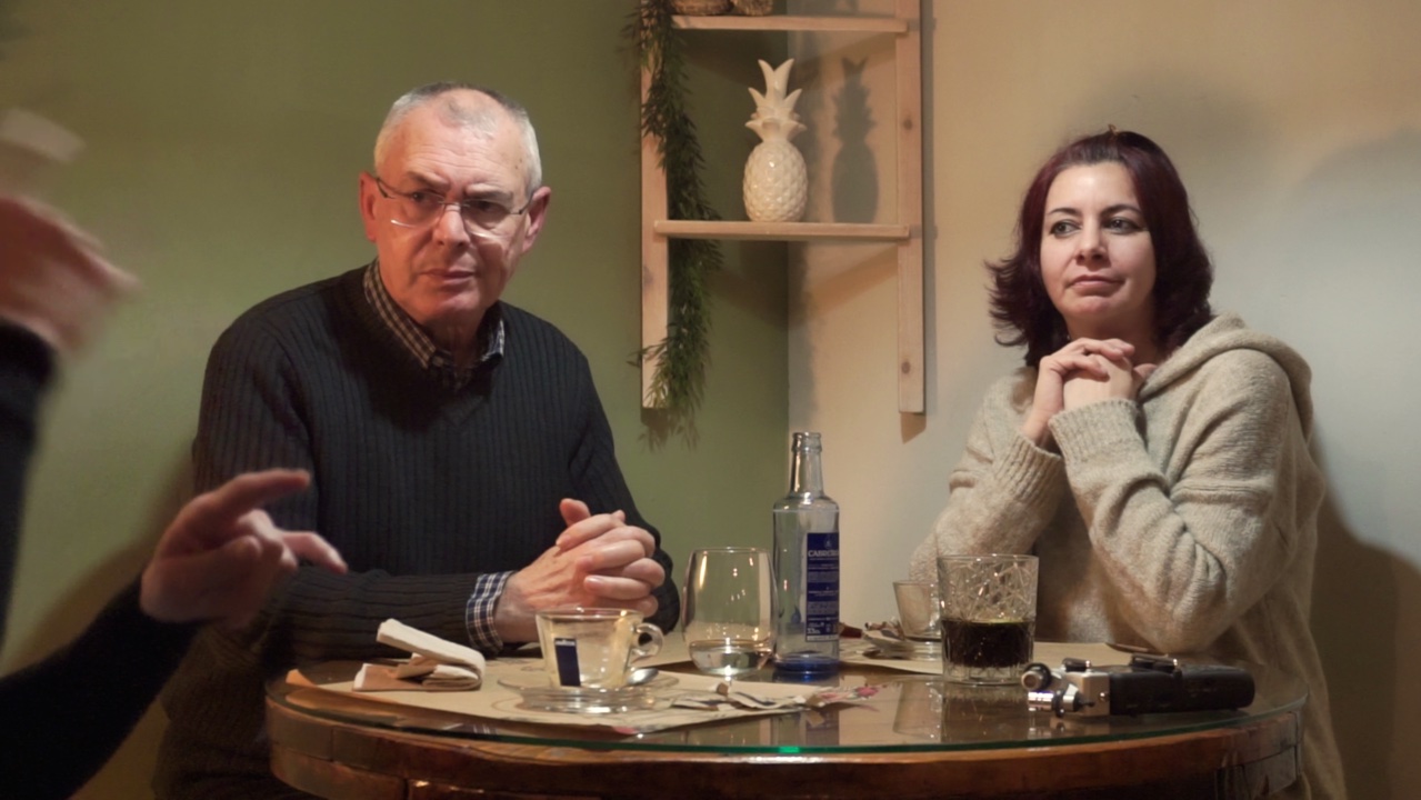 Mujer y hombre observan a otra persona signando sentados en la mesa de un restaurante. 