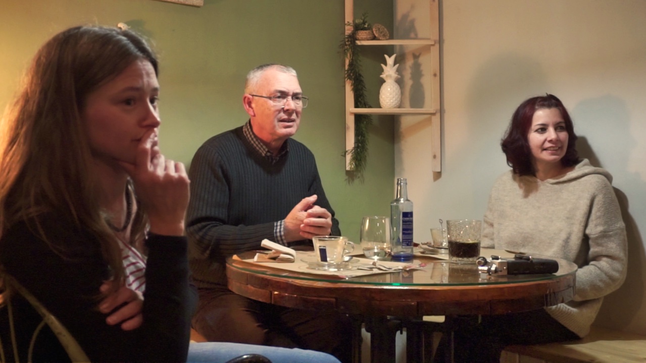 Dos mujeres y un hombre observan a alguien que les comenta algo. 